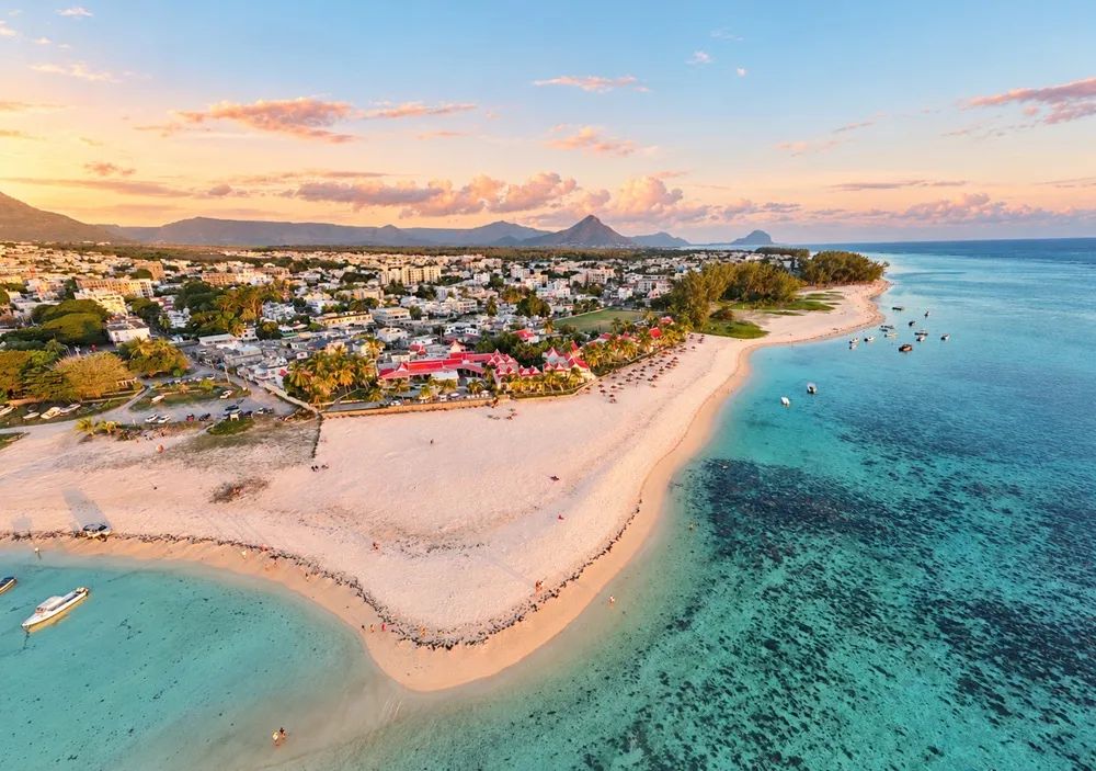 1. Red-roofed Villas Caroline hotel beside Flic en Flac Beach, with boats offshore and mountains in the distance.