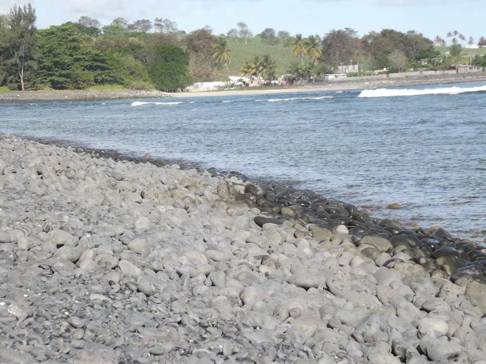 Waves breaking against rounded stones at Rivière des Galets beach, Mauritius.
